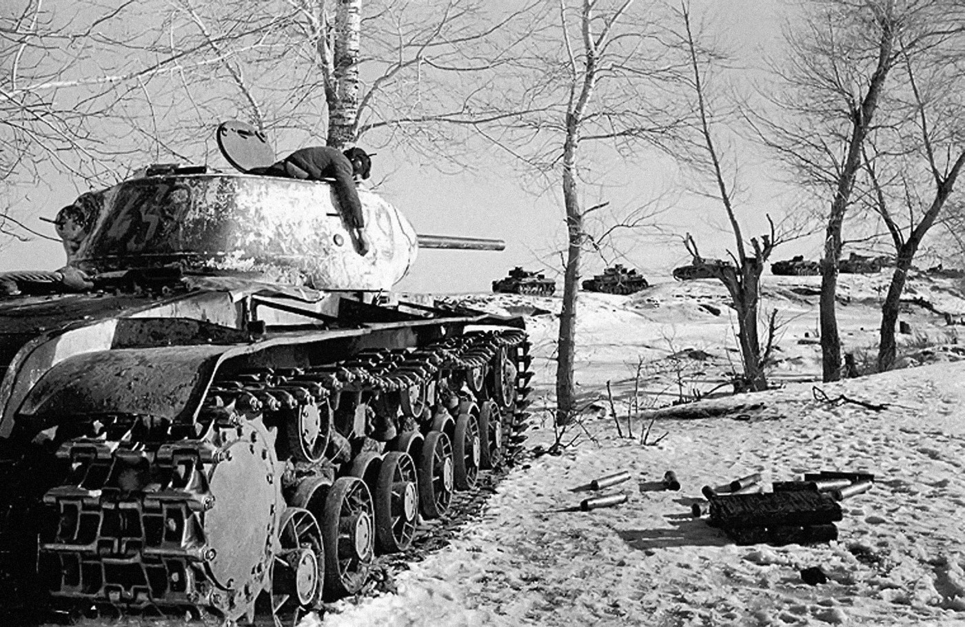 A knocked out KV-1S circa 1943, with the dead commander hanging from his cupola. It had just engaged the German column in the background.
